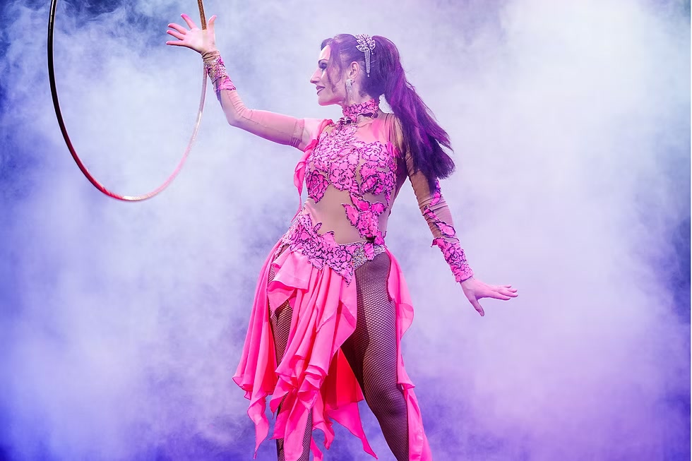 Anouchka Bouglione en costume fuchsia, faisant tourner un cerceau sur une piste éclairée de violet