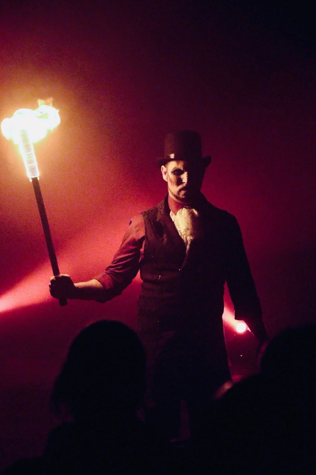 Personnage au chapeau haut de forme tenant une torche en flammes, dans la fumée rouge